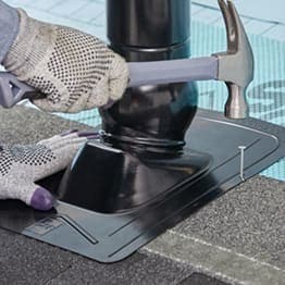 Contractor with hammer nailing the GAF Master Flow Pivot Pipe Boot Flashing in place.